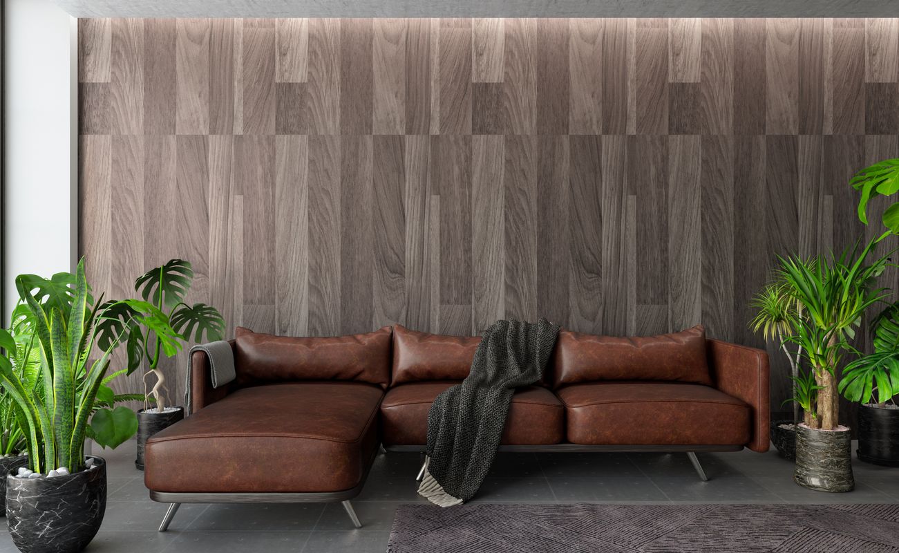 Ein modernes Wohnzimmer mit einer braunen Ledercouch, einem grauen Teppich und vielen Pflanzen vor einer Holzvertäfelung.